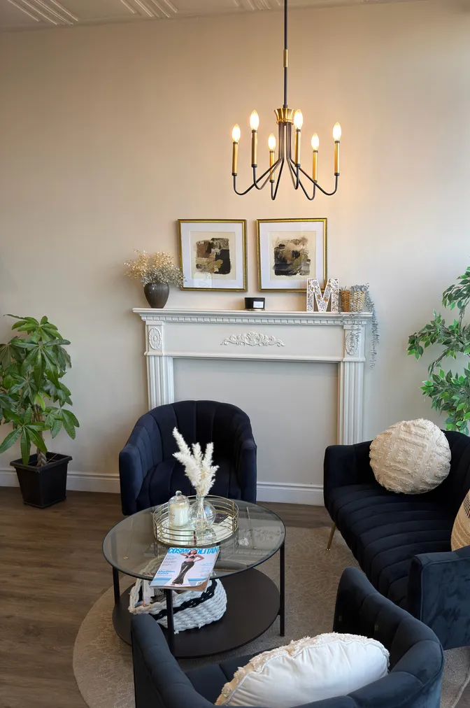 Waiting area at Modern Touch Beauty Salon, with navy velvet armchairs, a chandelier and a white mantel